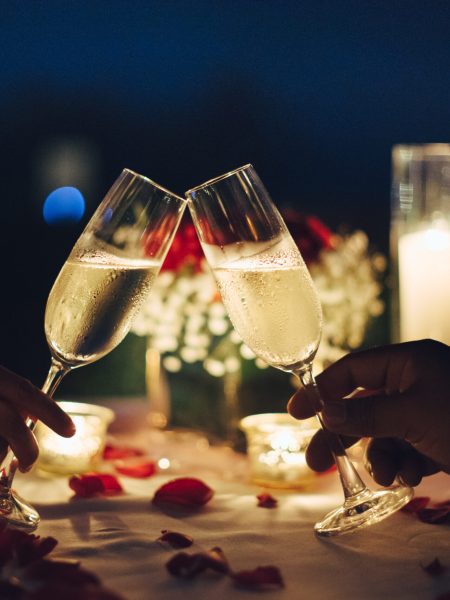 Romantic candlelight dinner table setup. Man & Woman hold glass of Champaign.